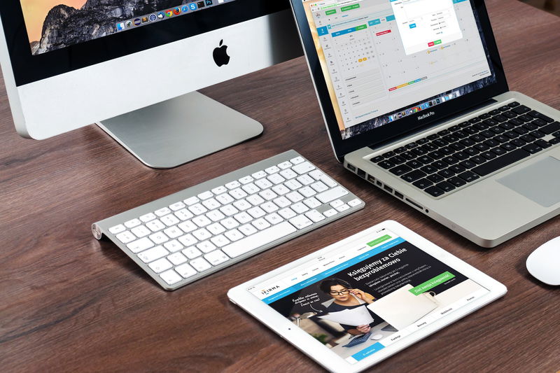 A desk with an iMac, MacBook, keyboard, mouse, and a tablet displaying various apps and websites invites creativity and focus. Sketch your ideas or draw inspiration from the vibrant digital workspace.