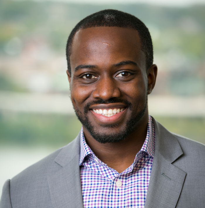 A man in a gray suit and checkered shirt smiles confidently, embodying the spirit of being climate resilient, as he stands against a blurred background.