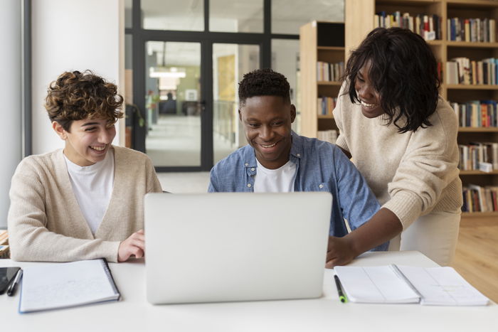 A diverse group of community college students collaborating in front of a laptop in a library.