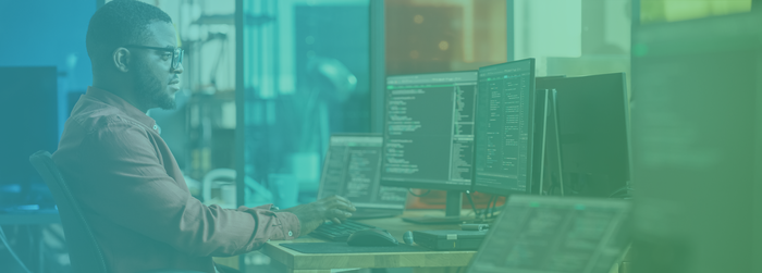 A person is working at a desk with multiple computer monitors displaying code in a tech office environment.