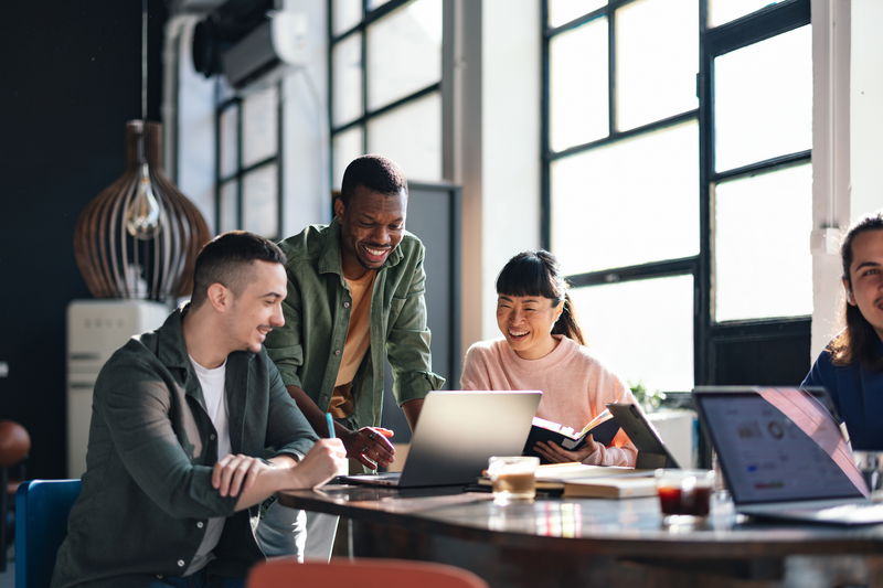 Diverse group of young adults engaged in a project, working together in a bright, contemporary co-working space, embodying teamwork and cooperation.