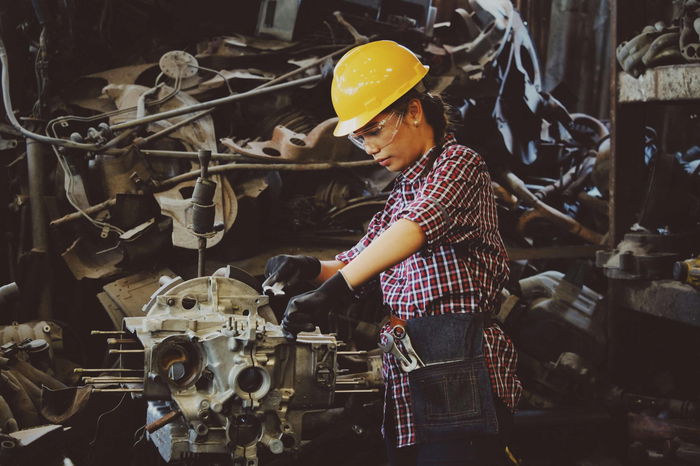 A person wearing a yellow hard hat and plaid shirt works on machinery in an industrial setting.