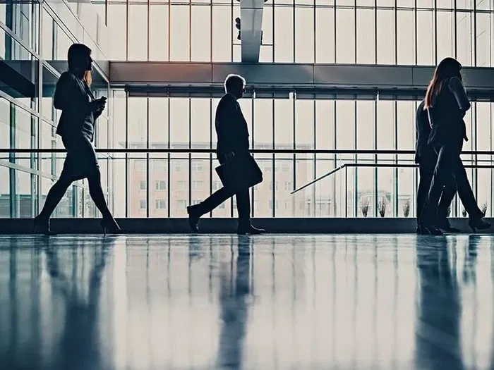 Silhouettes of people walking in an office building with large windows.