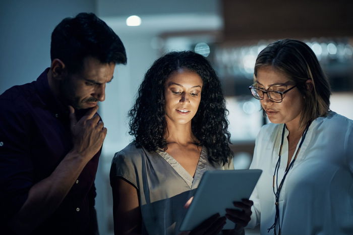 Three people looking at a tablet screen in a dimly lit environment.