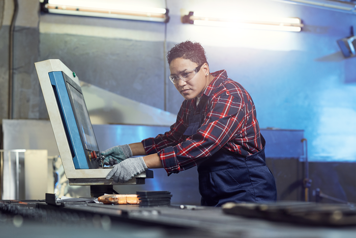 A worker wearing safety goggles operating a large piece machinery in an industrial environment