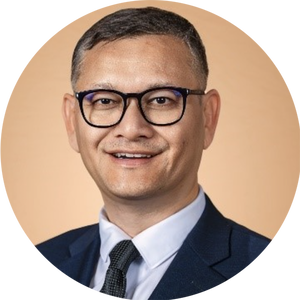 A person wearing glasses and a suit smiles against a plain background.