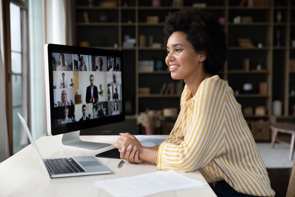 A woman in a striped shirt participates in a video conference on a computer at a desk.