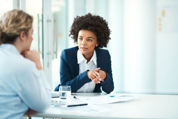 Two people having a discussion at a table with documents and a glass of water.