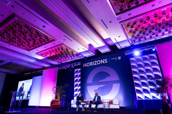 Two people sitting on stage in armchairs having a conversation at a conference called 