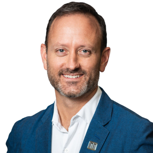 Dan is wearing a blue blazer and white shirt, smiling at the camera against a white background. He has short brown hair and a beard.