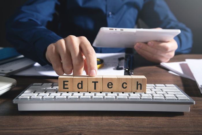 A person uses a tablet at a desk; wooden blocks spelling 