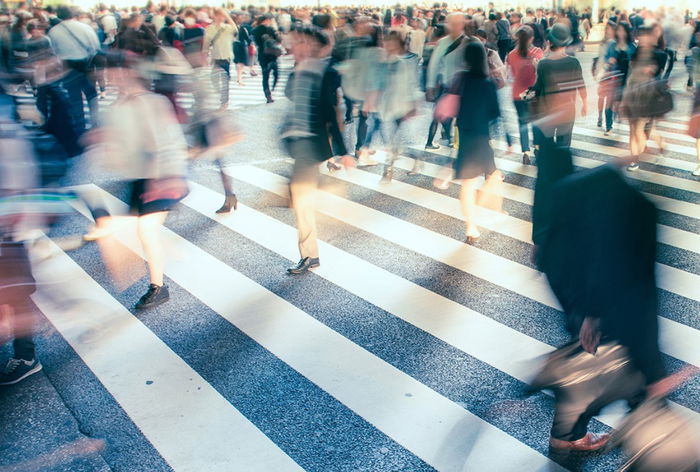 A large crowd of people crossing a city street at a crosswalk, with motion blur indicating movement.